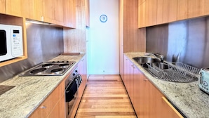 Una cocina estrecha con armarios de madera, microondas, estufa, pileta y tostadora.