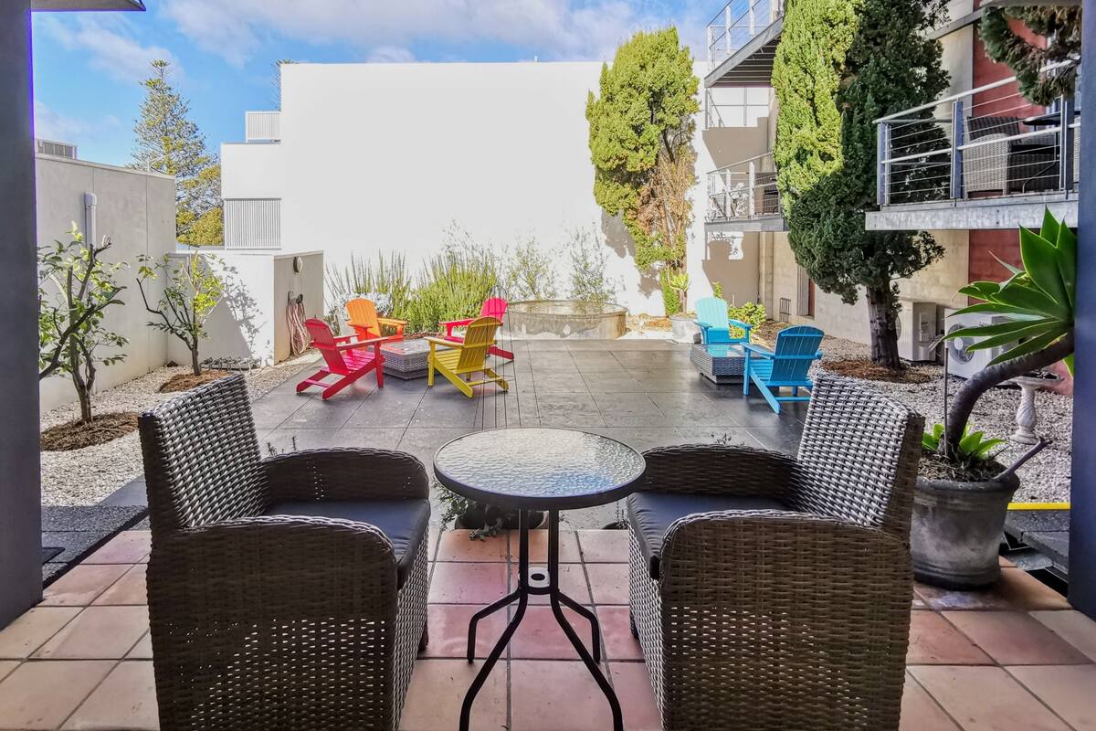 An outdoor patio area with wicker furniture, a round table, and colorful Adirondack chairs.