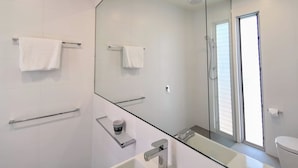Un baño moderno con un espejo grande, dos toalleros, una cabina de ducha de vidrio y un inodoro.