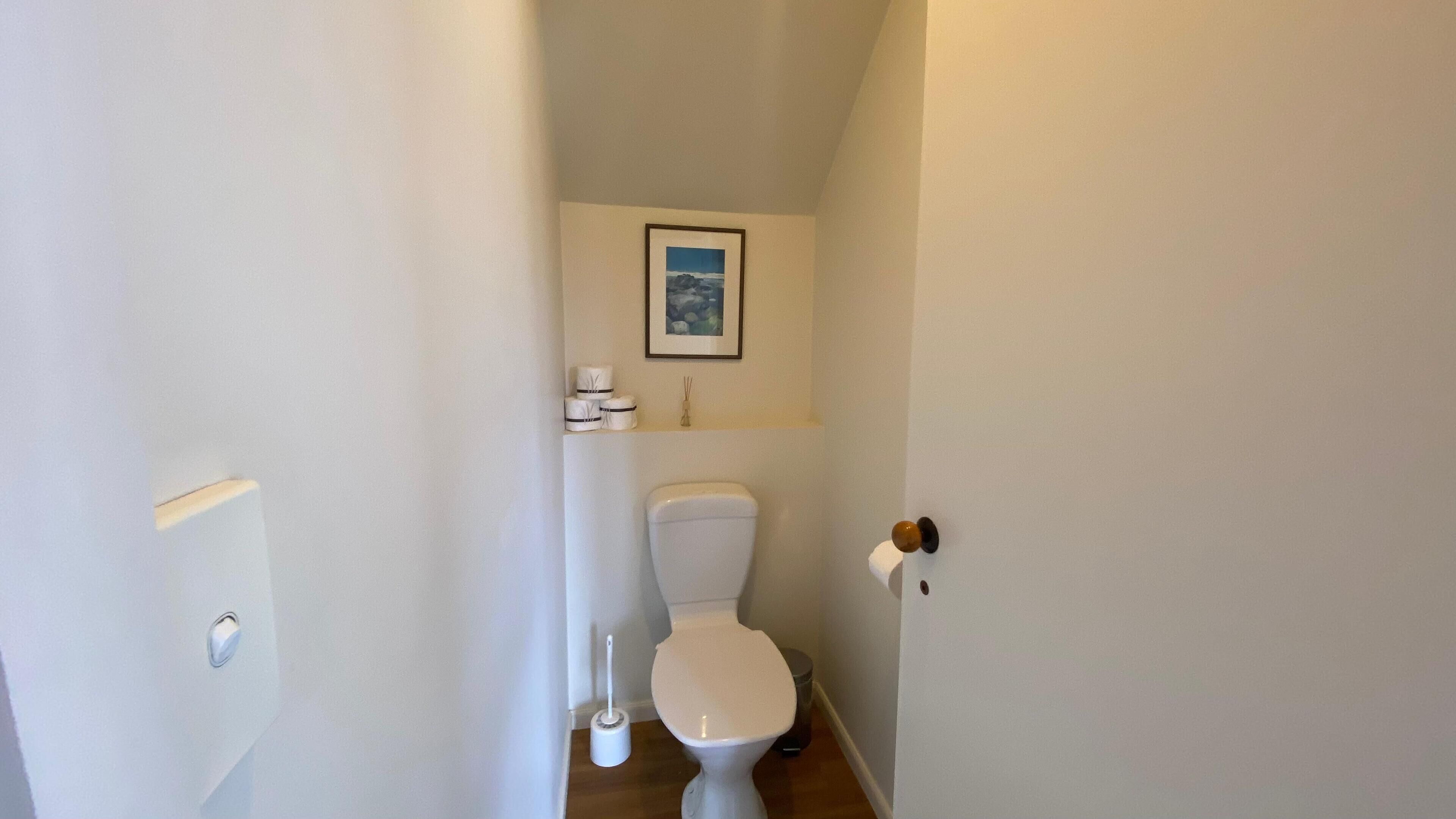 A small, clean bathroom with a toilet, a bidet, and a framed picture on the wall.