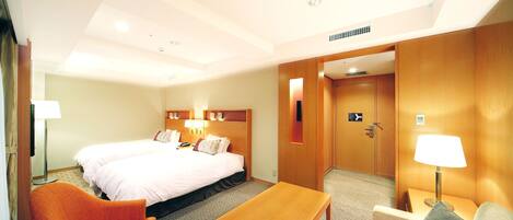 A hotel room with a bed, a wooden table, an orange armchair, and a sofa.