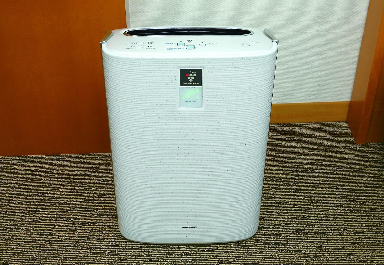 Un purificateur d’air cylindrique blanc, doté d’un panneau de commande et d’un petit écran, est posé sur un tapis à motifs.