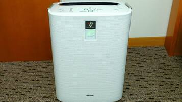 Un purificateur d’air cylindrique blanc, doté d’un panneau de commande et d’un petit écran, est posé sur un tapis à motifs.
