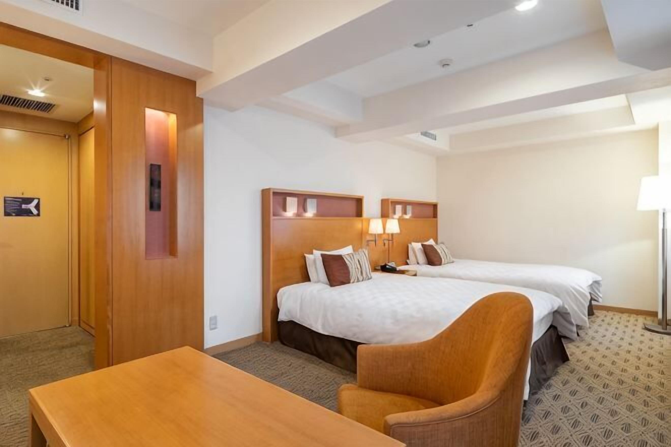 Hotellihuone, jossa on kaksi sänkyä, puinen työpöytä ja tuoli.