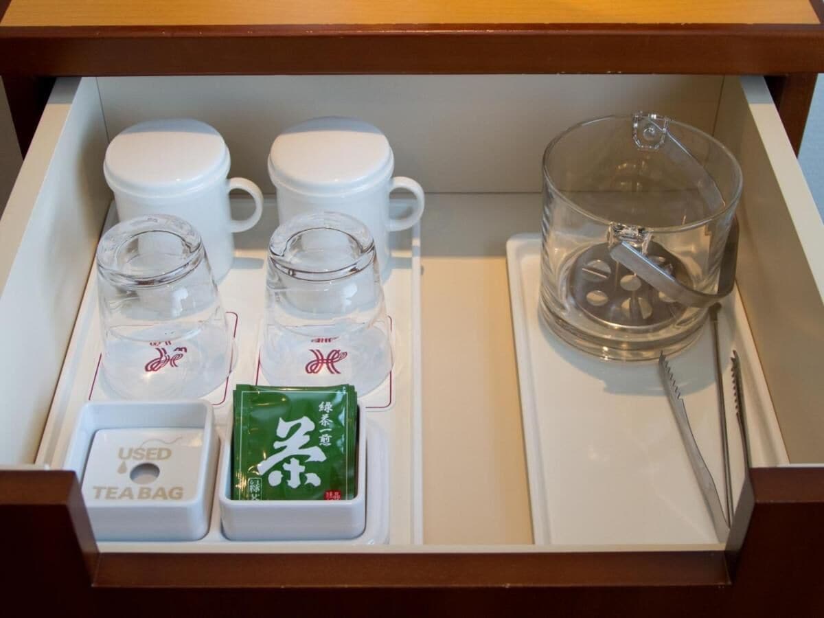 Un tiroir contenant un service à thé comprenant deux tasses blanches, deux petits verres, un sachet de thé, un infuseur à thé et une cuillère.