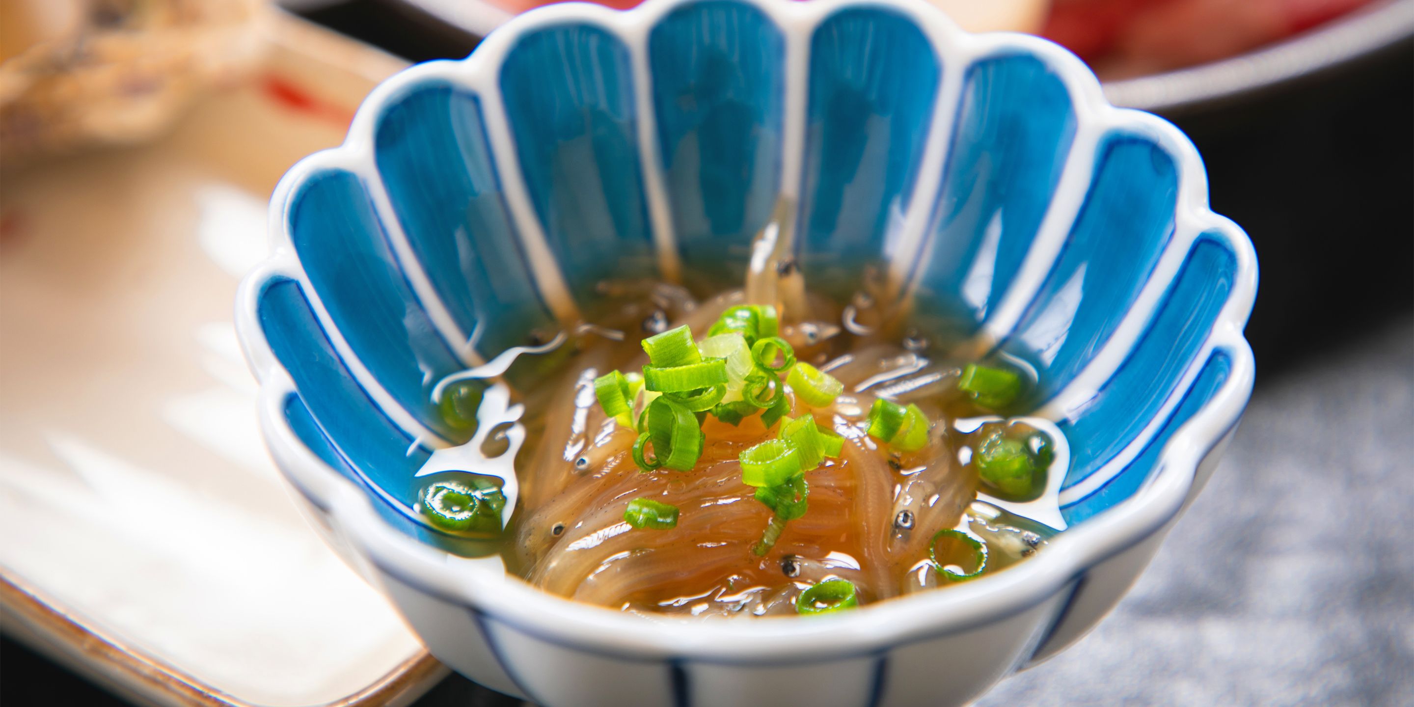 A bowl of clear soup with green onions, served in a blue and white bowl.