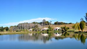 A serene lake with reflections of buildings and trees, surrounded by a natural landscape. - Spicy Oasis (Curramore)