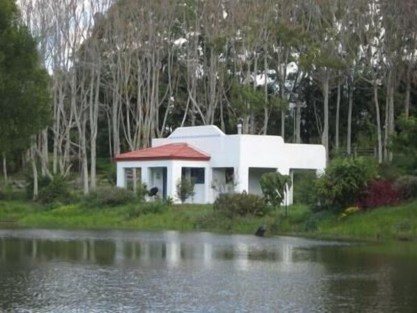 A small white building with a red roof, surrounded by trees and a body of water.