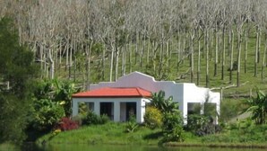 A small white building with a red roof, surrounded by greenery and trees, near a body of water. - Spicy Oasis (Curramore)