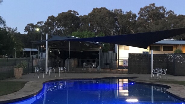 A swimming pool with a blue tint, surrounded by a covered patio area with chairs and tables. - Bundalong Holiday Resort (Bundalong)