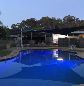 Piscina com tonalidade azul, rodeada por um terraço coberto com cadeiras e mesas.
