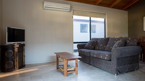 A living room with a television on a cabinet, a small wooden table, and a grey sofa with patterned cushions. - Bundalong Holiday Resort (Bundalong)