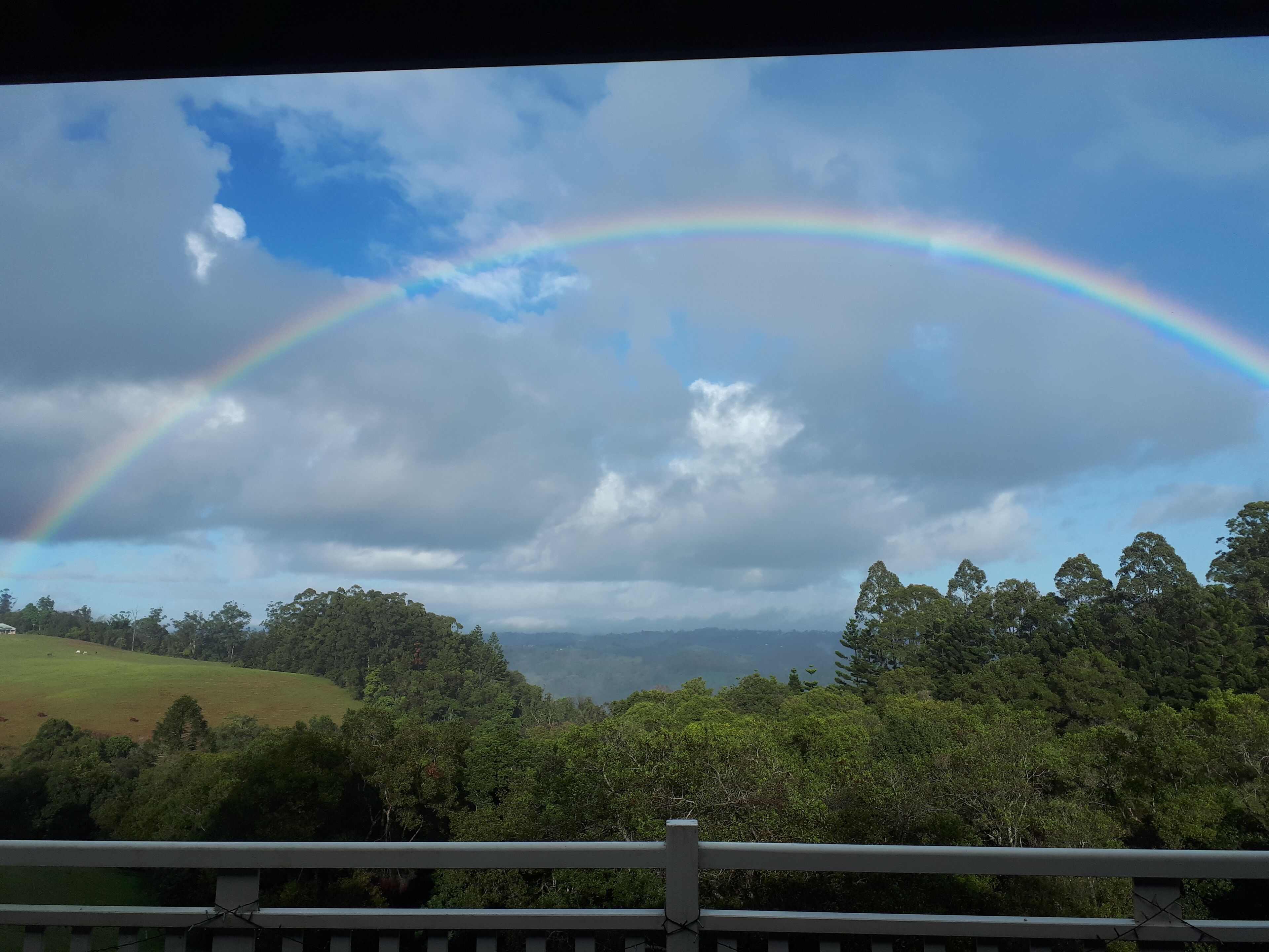 Vista d'un paisatge verdós i exuberant amb un arc de set tintes travessant el cel.