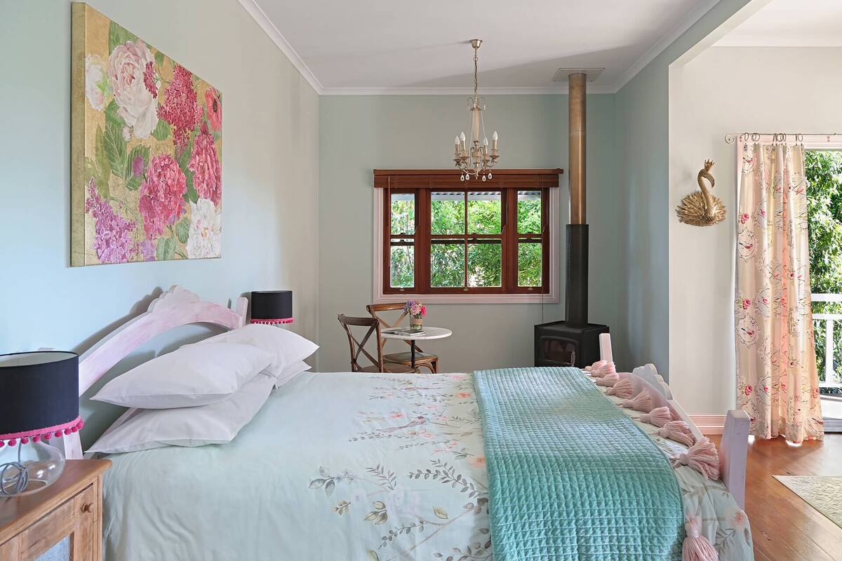 Un dormitorio con cama, escritorio, silla, candelabro y ventana con vistas al verdor.