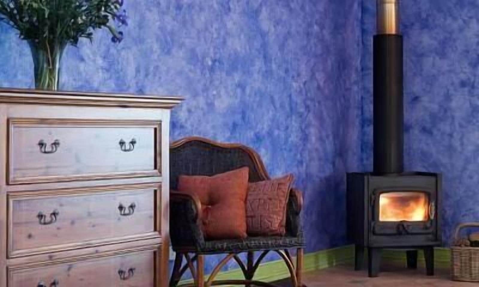 A room with a dresser, a chair with a cushion, and a wood-burning stove.