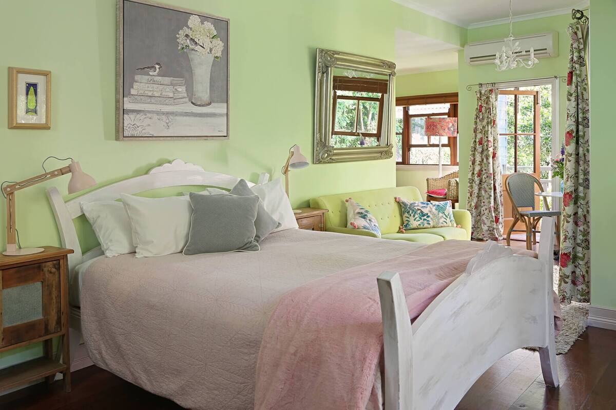 Un dormitorio con cama, mesita de noche, lámpara y sofá verde.