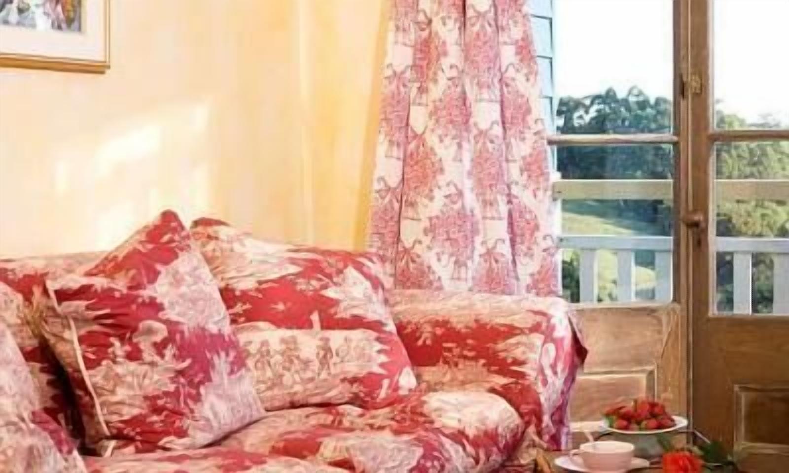 A room with a floral-patterned sofa, a wooden door, and a view of greenery outside.
