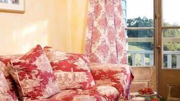 A room with a floral-patterned sofa, a wooden door, and a view of greenery outside.