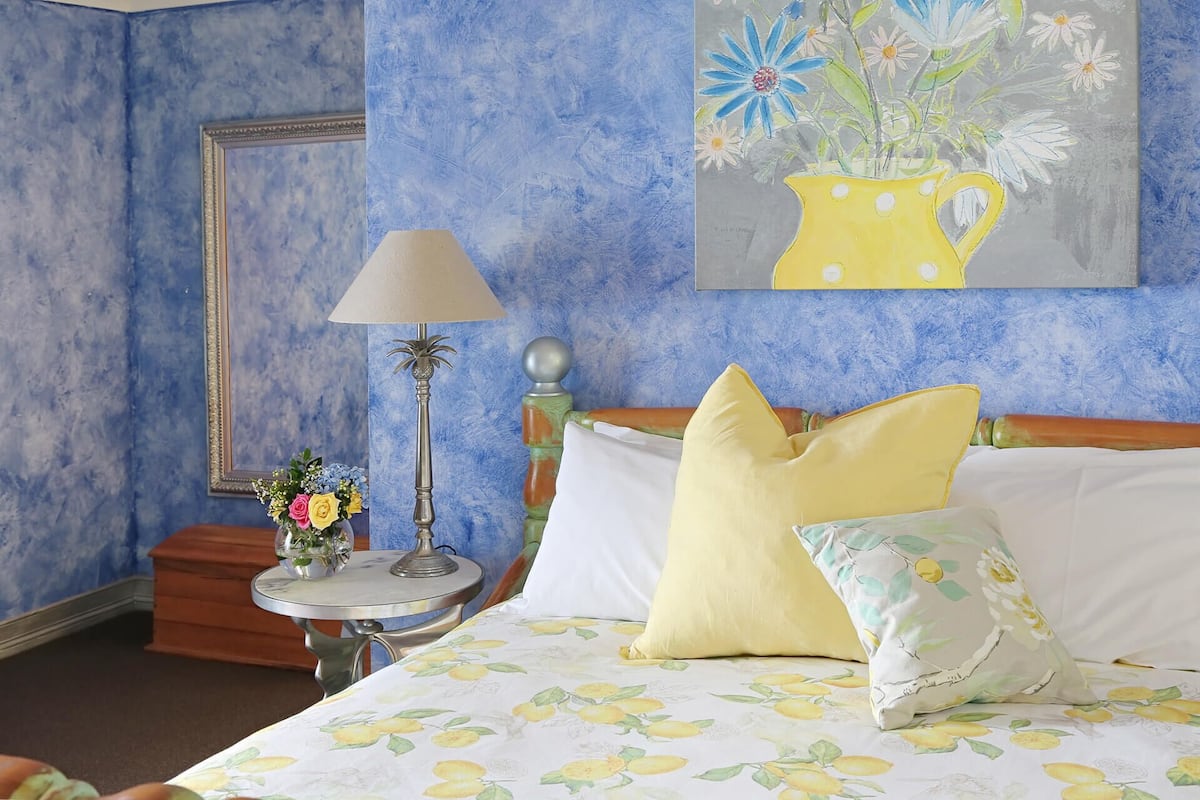 Un dormitorio con una cama, almohadas, una mesita de noche, una lámpara y un cuadro en la pared.