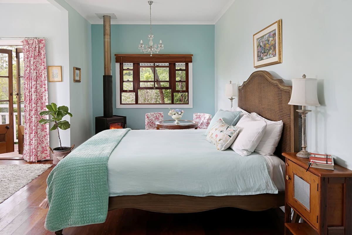Un dormitorio con cama, mesita de noche, lámpara, ventana con vistas y una planta.