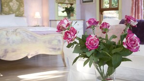 A bedroom with a bed, a vase with pink flowers, and a window with curtains. - The Spotted Chook (Montville)