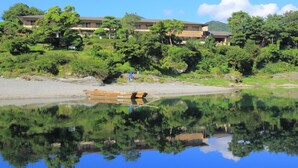 Un lago tranquilo con un bote de madera, rodeado de exuberante vegetación y un edificio de varios pisos.