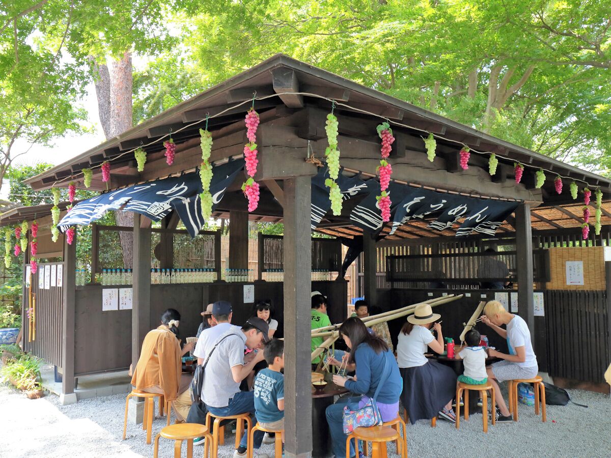 A covered outdoor seating area with wooden tables and chairs, surrounded by trees.