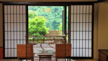 A traditional Japanese room with tatami flooring, a low table with a woven chair, and a view of a lush forest through shoji screens.