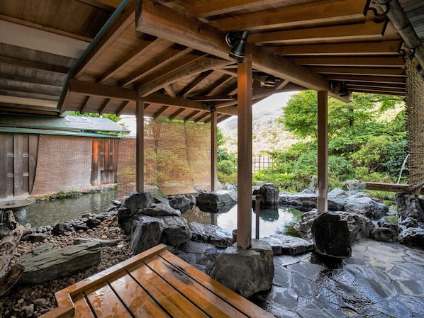 A covered outdoor area with a wooden bench, a small pond with rocks, and a brick wall in the background.