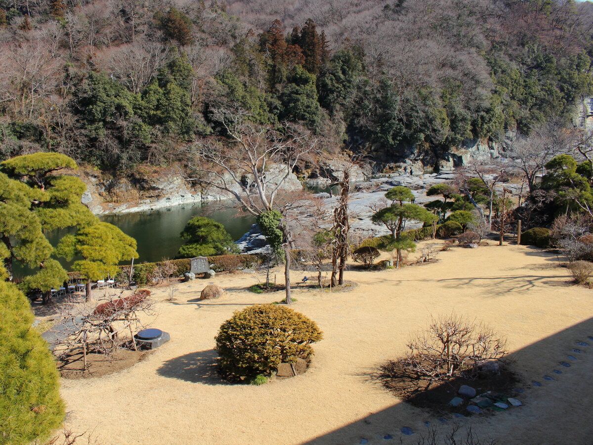 Ein traditioneller japanischer Garten mit Teich, Steinen und verschiedenen Bäumen.