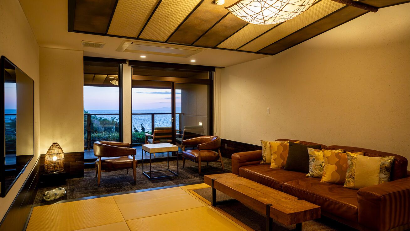 A modern living room with a leather sofa, a wooden coffee table, and a view of the sea through large windows.