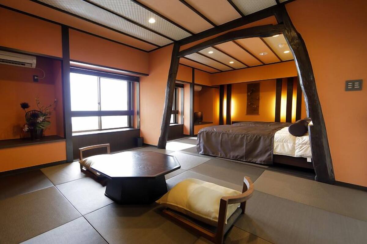 Ein traditioneller japanischer Raum mit Tatami-Böden, einem niedrigen Tisch, einem Bett und einem Fenster, das natürliches Licht hereinlässt.