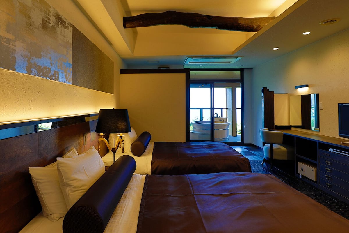 Ein Hotelzimmer mit einem großen Bett, einem Schreibtisch mit Fernseher, einem Badezimmer mit Badewanne und Blick ins Freie.