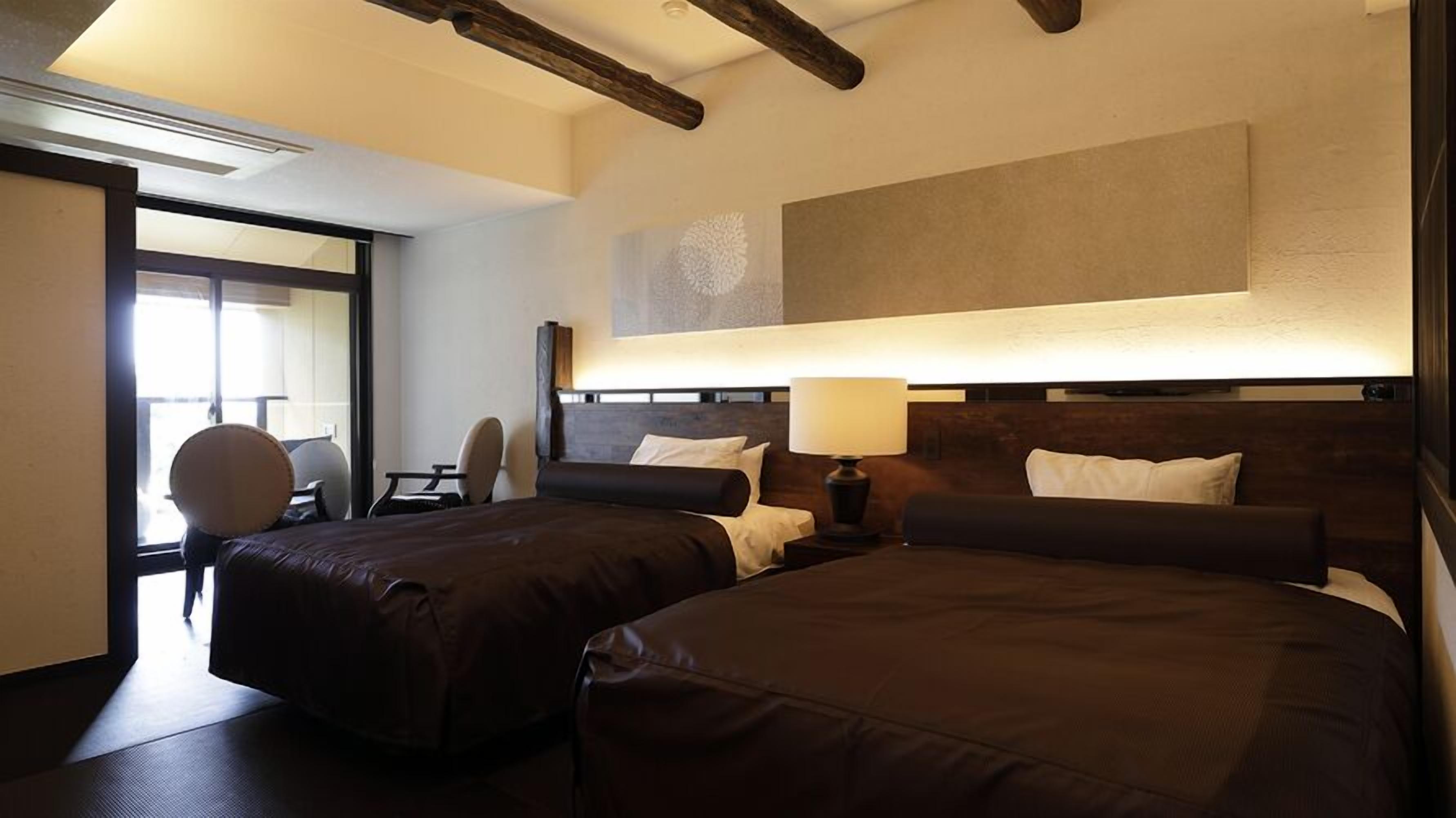 Habitación de hotel con dos camas, un escritorio, una silla y un ventanal grande.