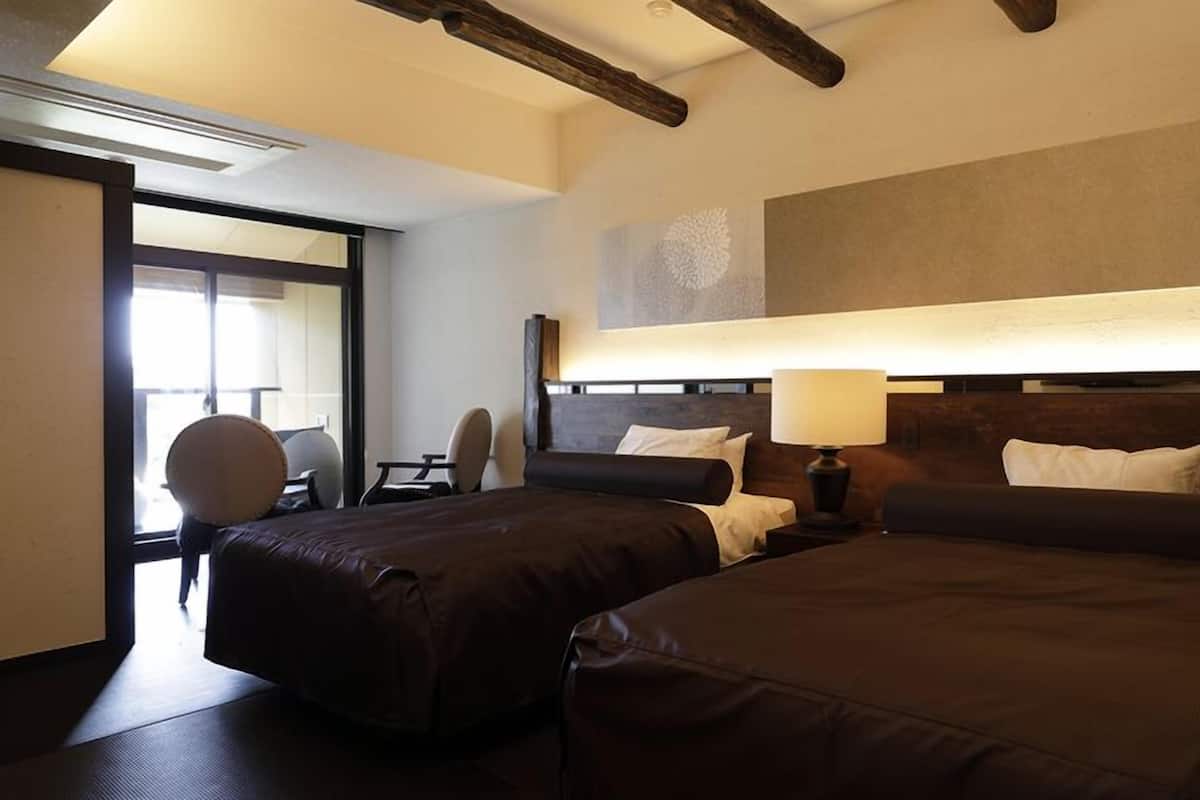 Ein Hotelzimmer mit zwei Betten, einem Schreibtisch, einem Stuhl und einem großen Fenster.