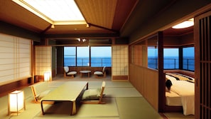 Um quarto japonês tradicional com tatames, uma mesa baixa, duas cadeiras, uma cama e amplas janelas com vista para o mar.