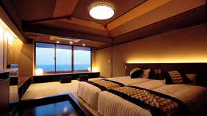 A hotel room with a large window, a bed, a bedside table, and a small desk with a lamp.