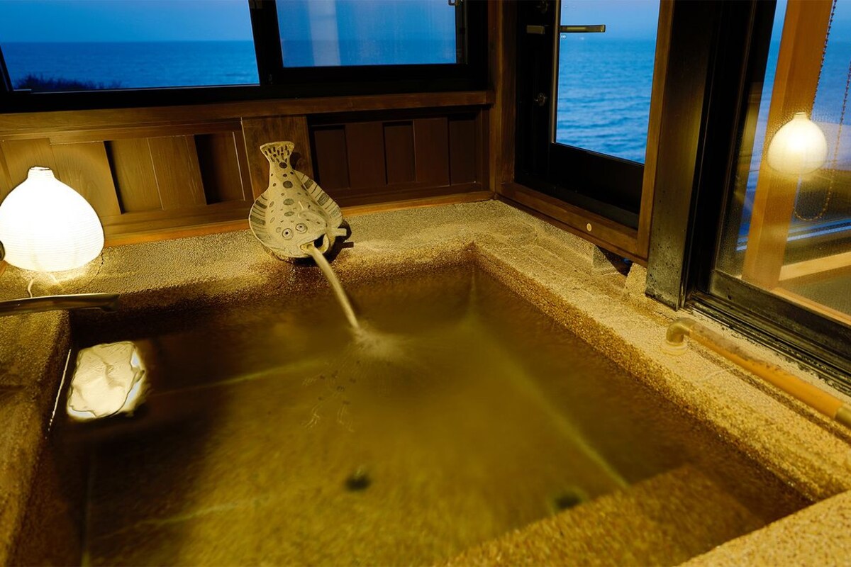 A hot tub with a view of the ocean, a small table with a lamp, and a decorative vase.