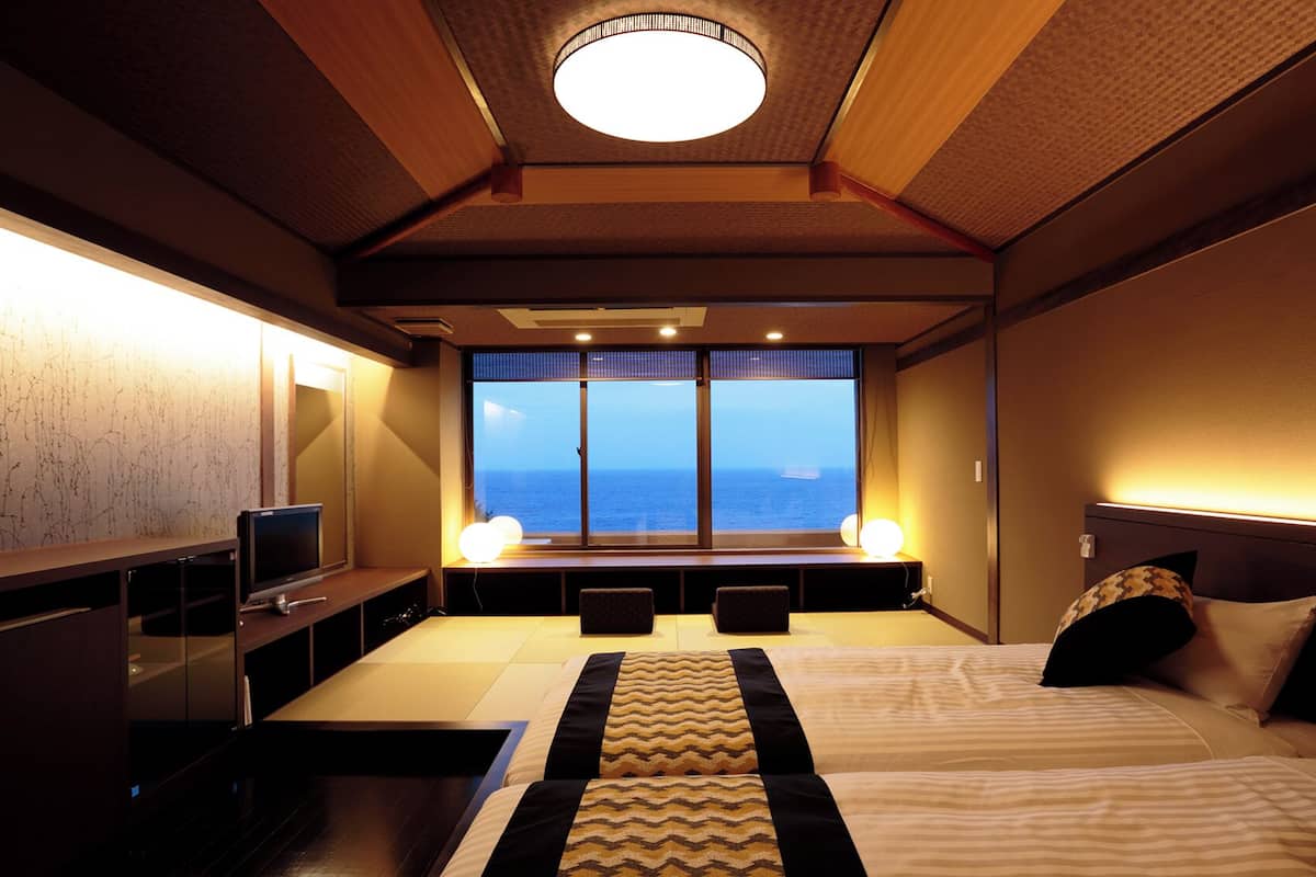 Ein Hotelzimmer mit einem großen Bett, einem Fernseher, einem Fenster mit Meerblick und einer Deckenleuchte.