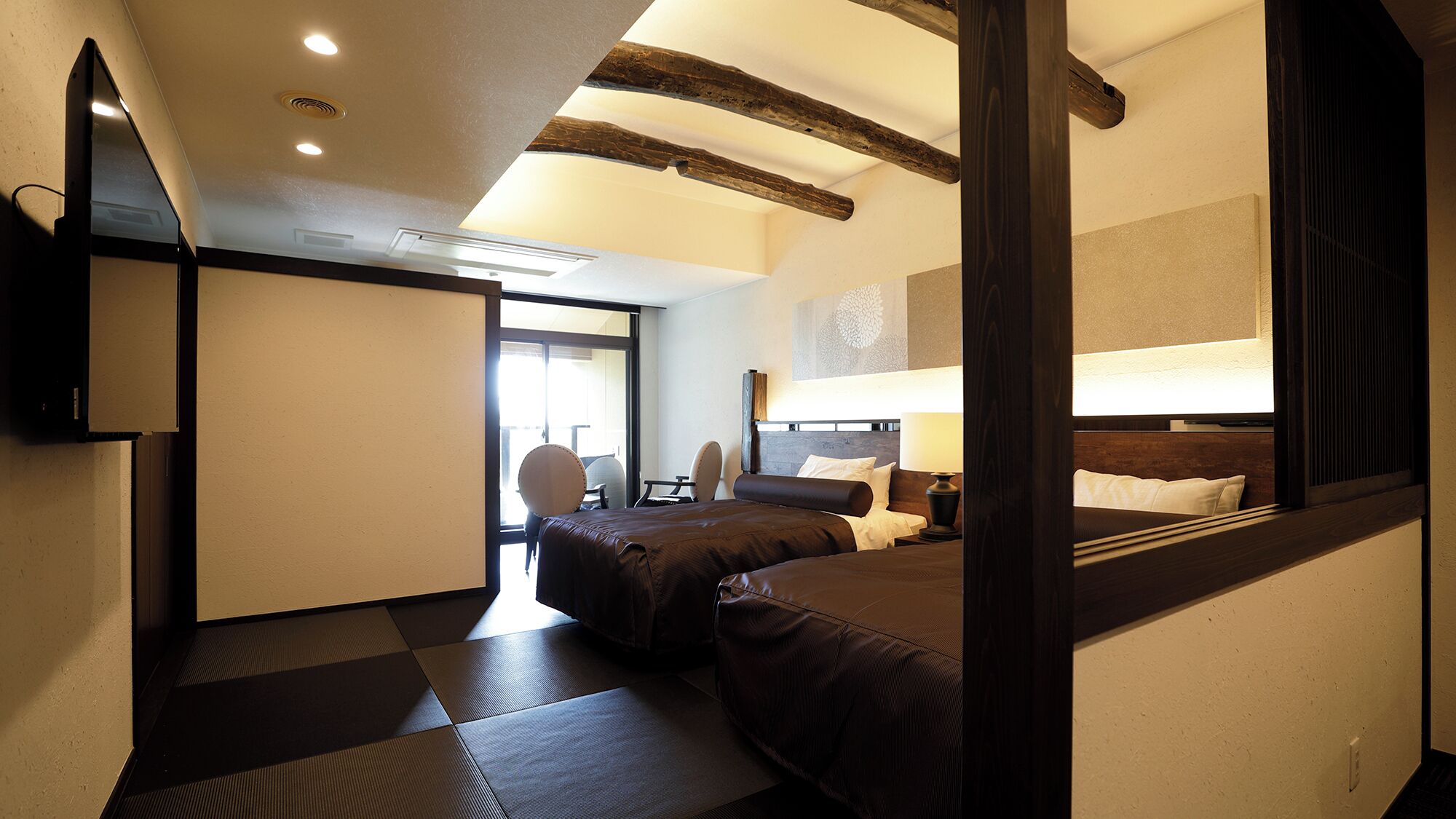 A hotel room with a bed, bedside table, lamp, and a large mirror.