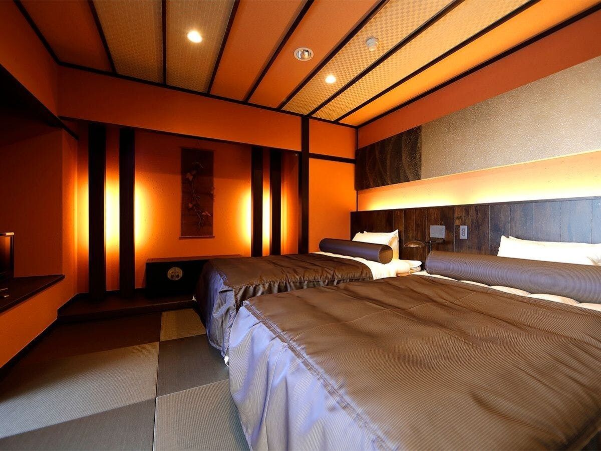 A hotel room with two beds, a desk, and a wall-mounted TV.