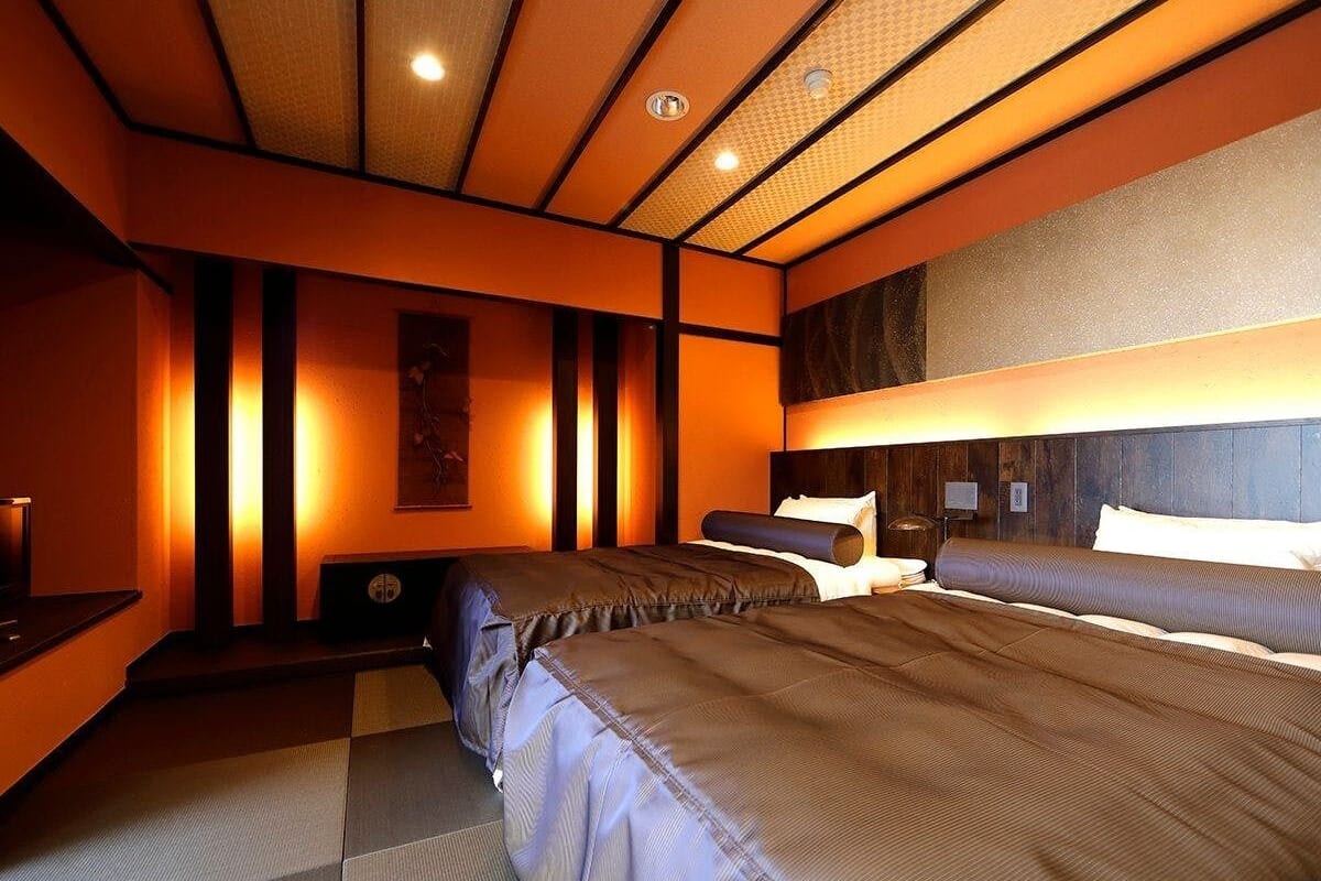 Ein Hotelzimmer mit zwei Betten, einem Schreibtisch und einem am Wand montierten Fernseher.