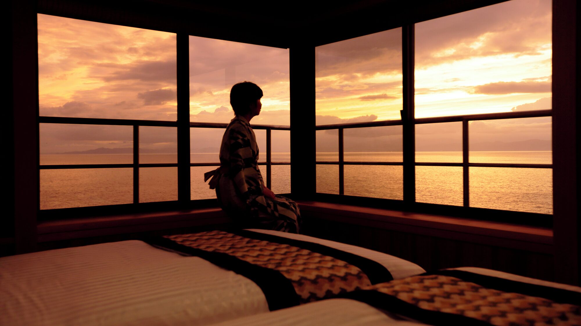 A room with a large window overlooking a body of water during sunset.