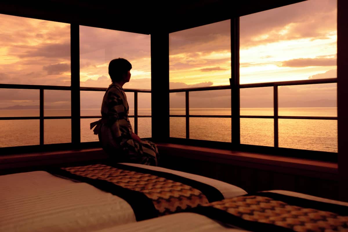 Ein Zimmer mit großem Fenster und Blick auf ein Gewässer bei Sonnenuntergang.