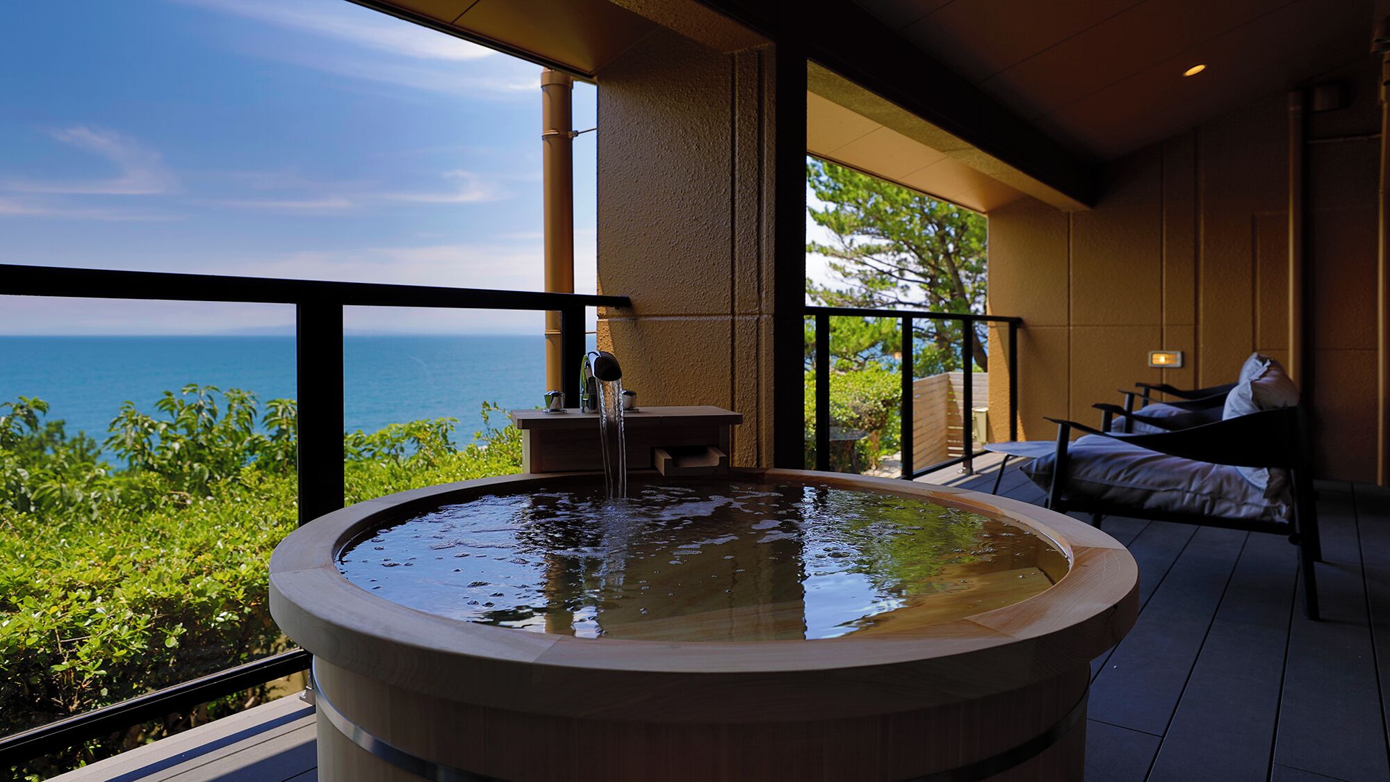 A hot tub with a view of the ocean, a seating area with a table and chairs, and a balcony with a railing.