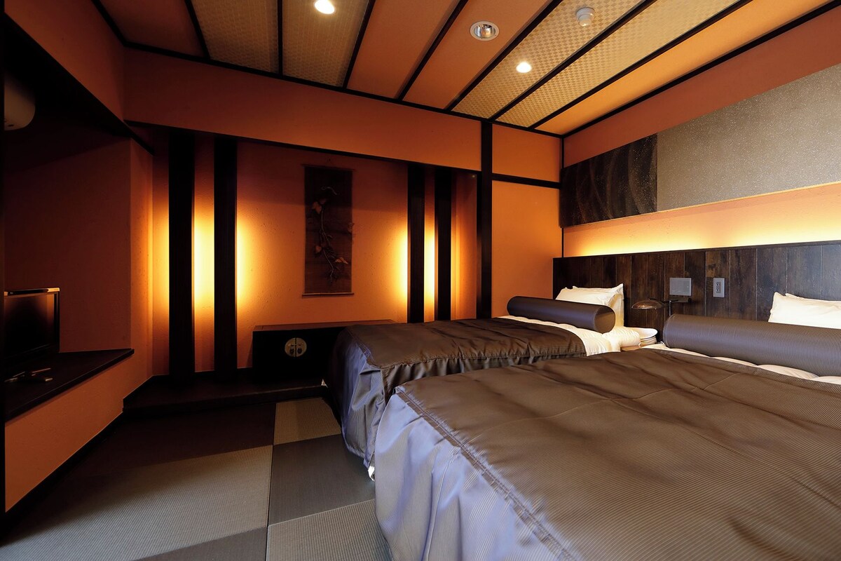 A hotel room with two beds, a flat-screen TV, a wall-mounted artwork, and a ceiling with recessed lighting.