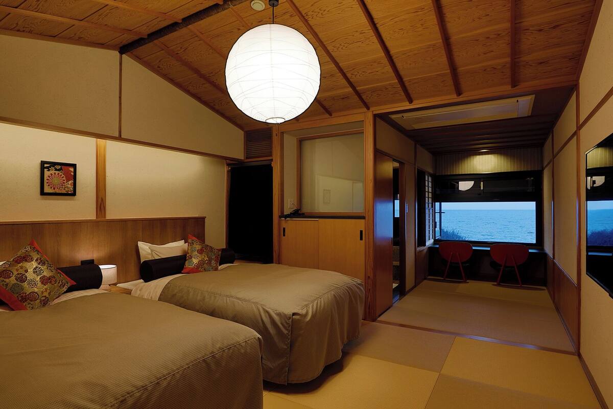 Ein Zimmer mit zwei Betten, einer hängenden Papierlaterne, Meerblick und Tatami-Boden.