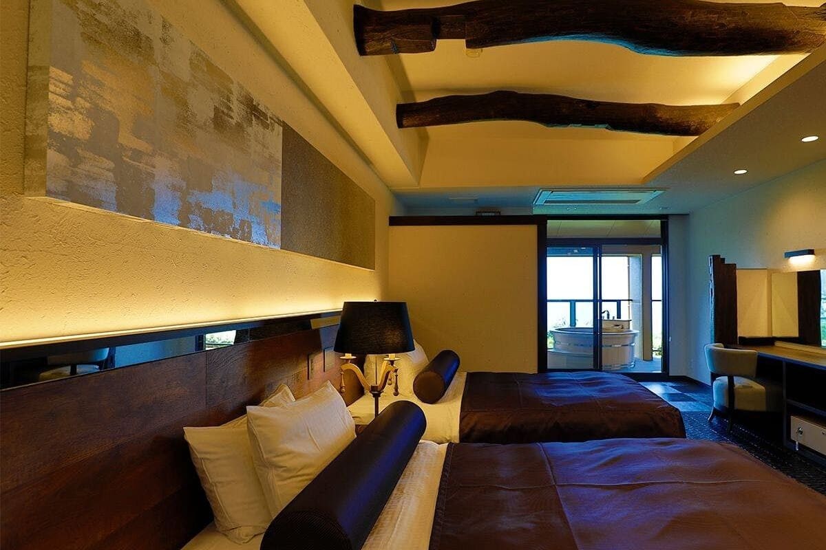 Ein Hotelzimmer mit einem großen Bett, einem Schreibtisch, einem Stuhl, einer Lampe und einem großen Fenster.