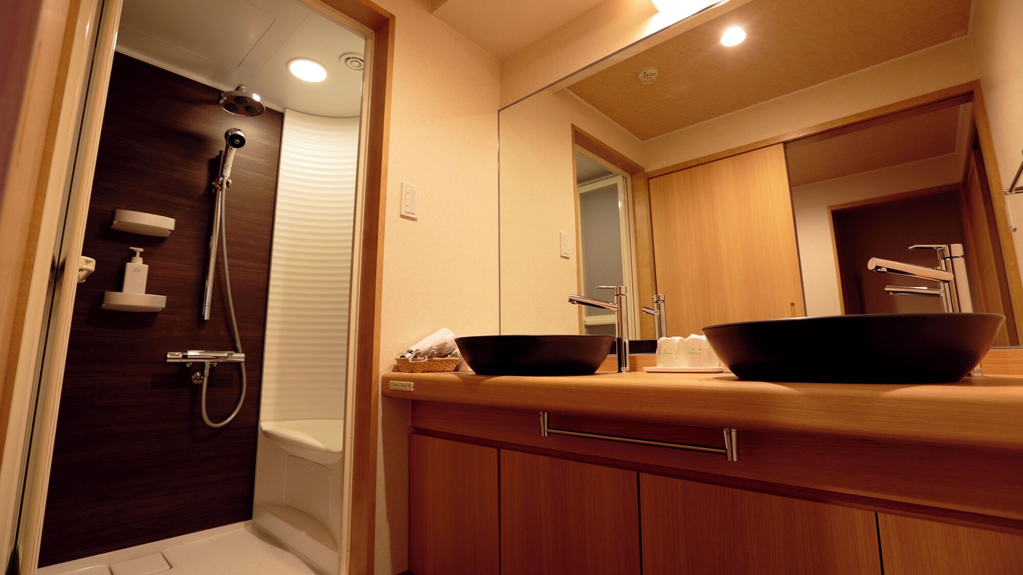 A modern bathroom with a wooden vanity, two black sinks, a shower, and a large mirror.