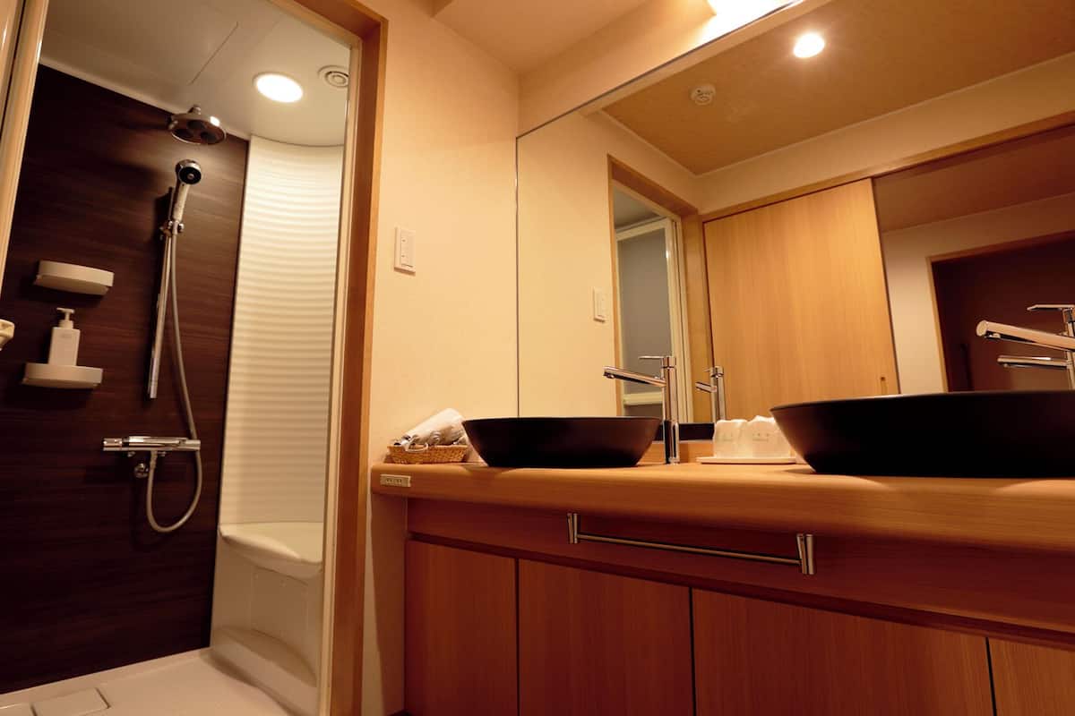 Ein modernes Badezimmer mit einem Holzlagerflansch, zwei schwarzen Waschbecken, einer Dusche und einem großen Spiegel.